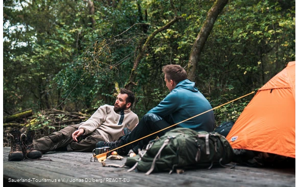 Zwei Wanderer sitzen auf einem Trekkingplatz im Wald