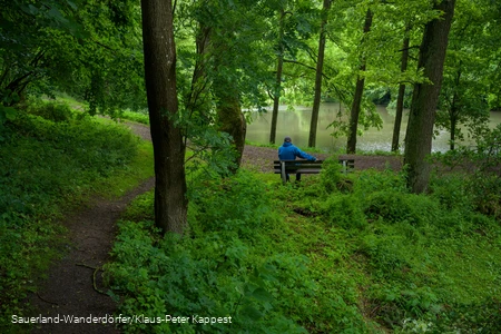 Ein Mann sitzt auf einer Parkbank am Teich vom Kloster Flechtorf