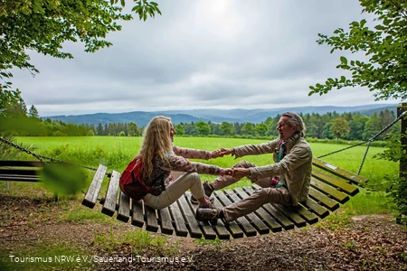 Eine Frau und ein Mann sitzen sich gegenüber auf einer großen Holzhängematte