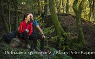 Zwei Rothaarsteig-Wanderer sitzen im grünen Wald auf einem Stein
